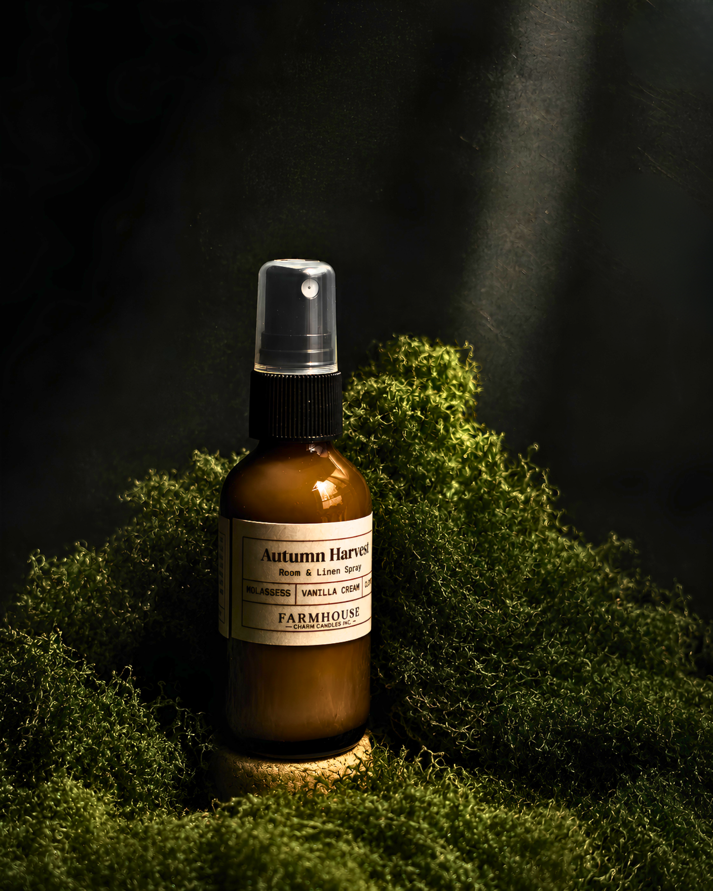 An amber glass spray bottle labeled 'Autumn Harvest' by Farmhouse Charm Candles , placed on a bed of green moss against a dark, moody background with dramatic light beams.