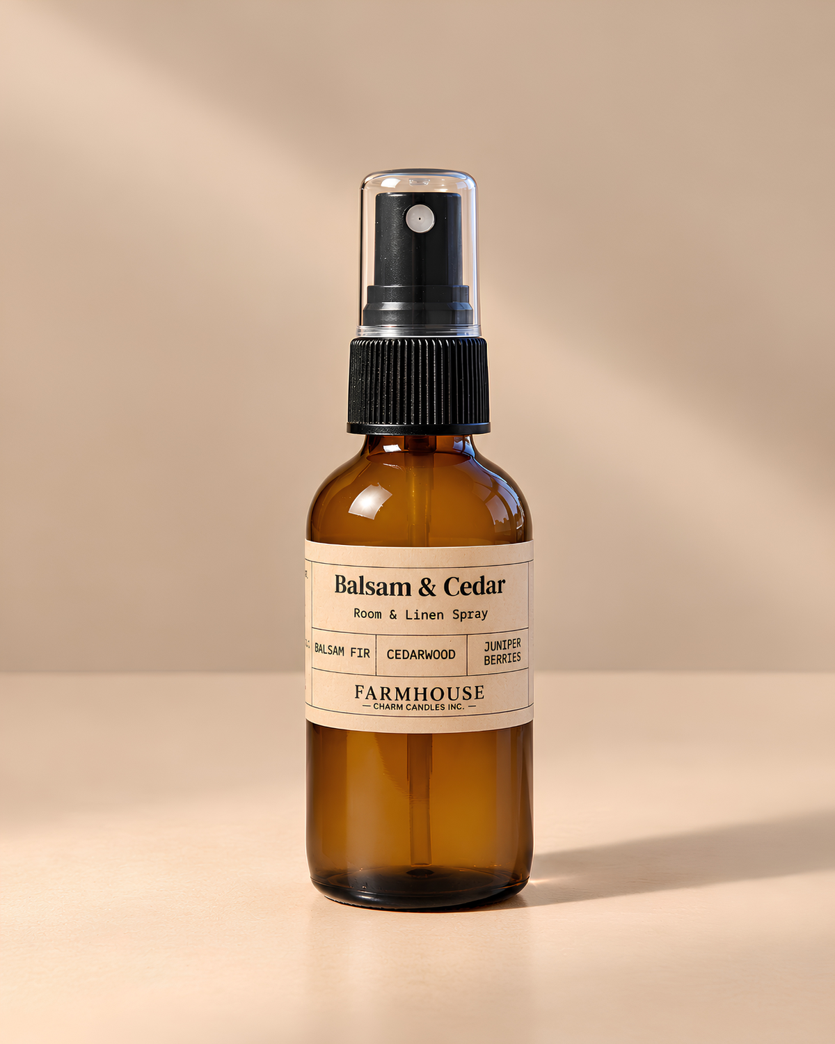 An amber glass room and linen spray bottle with a black spray top and a cream label reading 'Balsam & Cedar' and 'FARMHOUSE Charm Candles', photographed on a warm beige background with soft shadows.