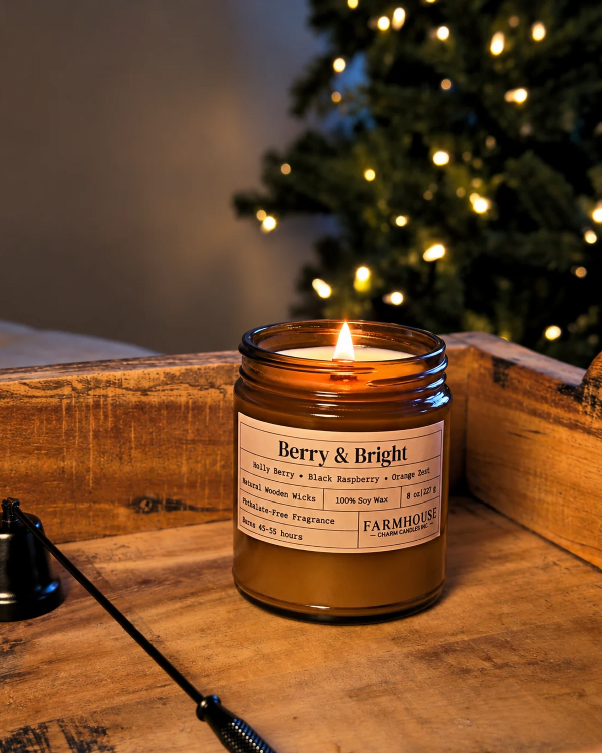 A lit amber glass jar candle labeled 'Berry & Bright' by Farmhouse Charm Candles, placed on a rustic wooden surface with a blurred Christmas tree in the background.