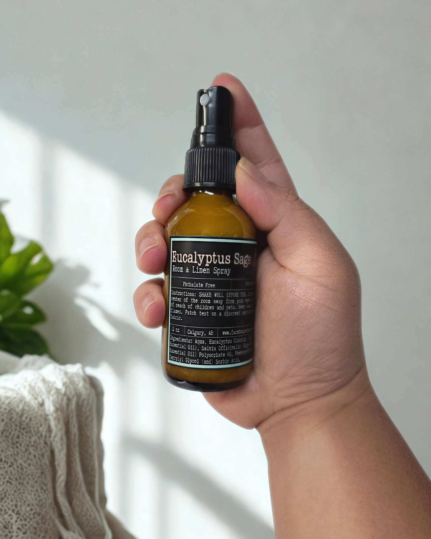 Hand holding a bottle of Eucalyptus Sage room & linen spray against a neutral background. Farmhouse Charm Candles