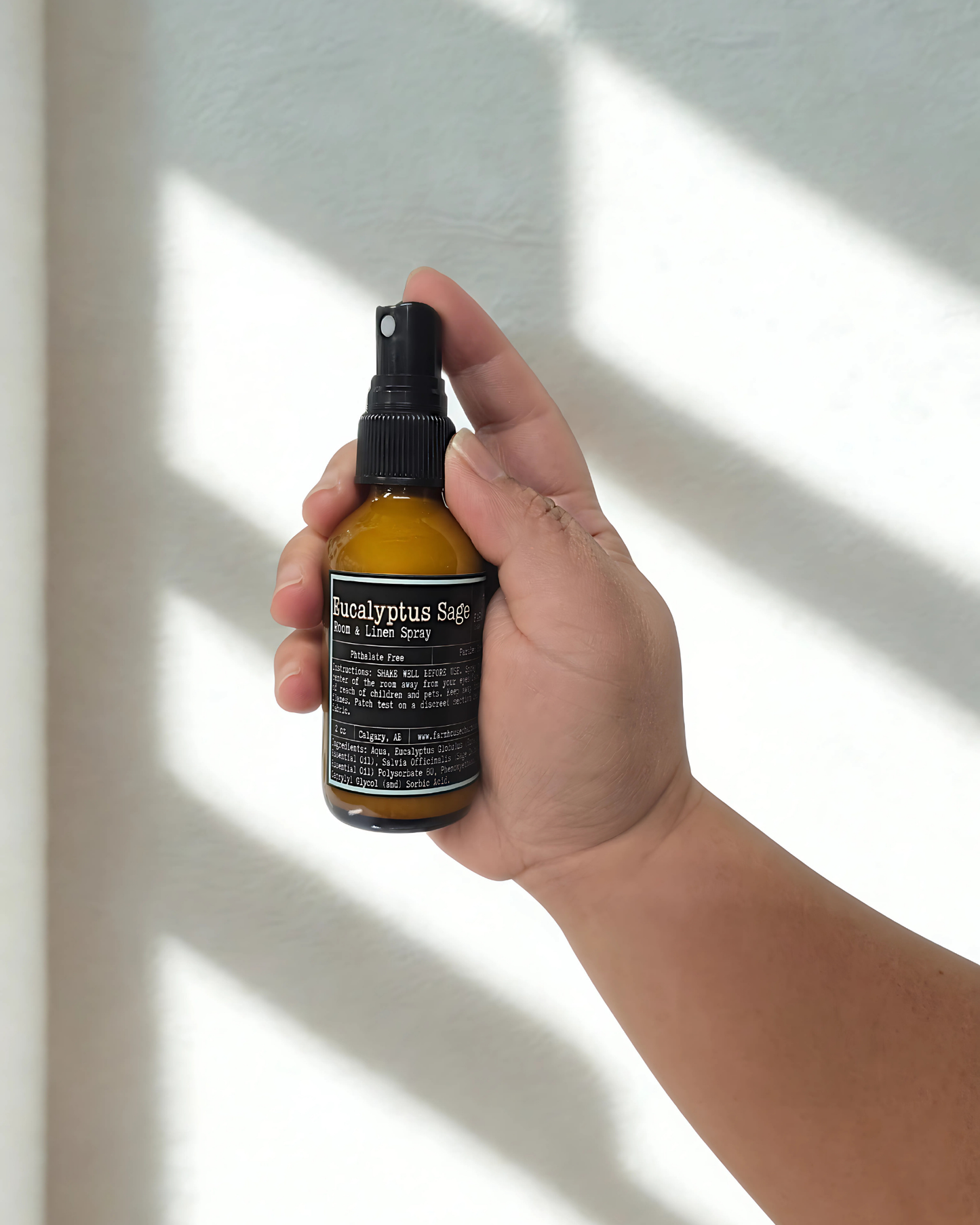 Hand holding a bottle of Eucalyptus Sage room & linen spray against a neutral background. Farmhouse Charm Candles