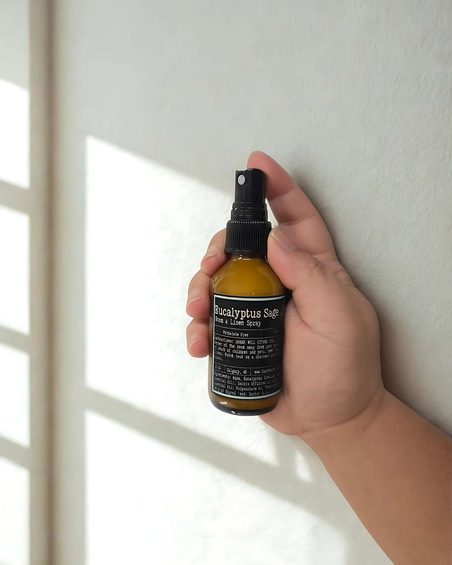 Hand holding a bottle of Eucalyptus Sage room & linen spray against a neutral background. Farmhouse Charm Candles