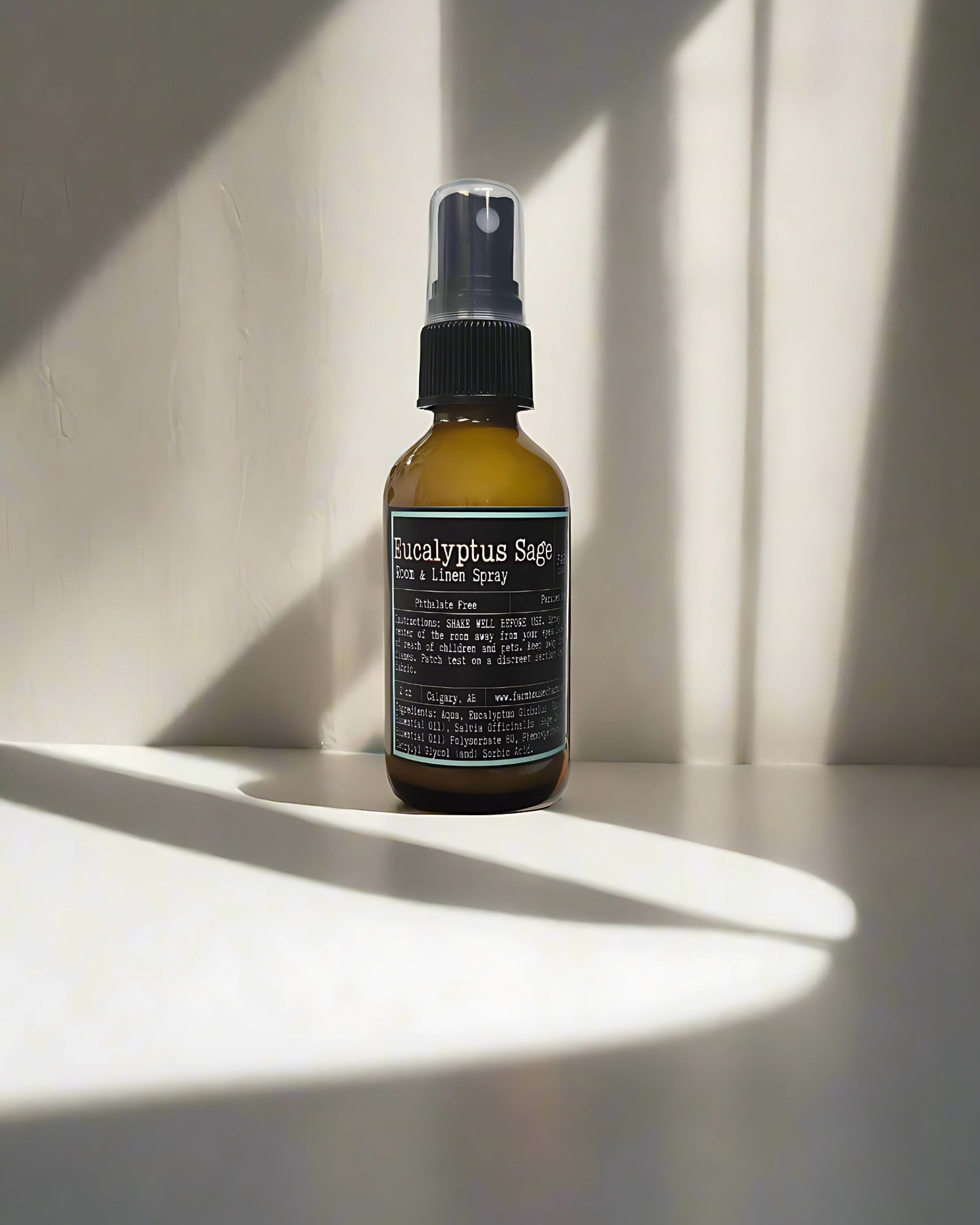 Bottle of eucalyptus sage room spray on a white surface with shadows cast by natural light. Farmhouse Charm Candles