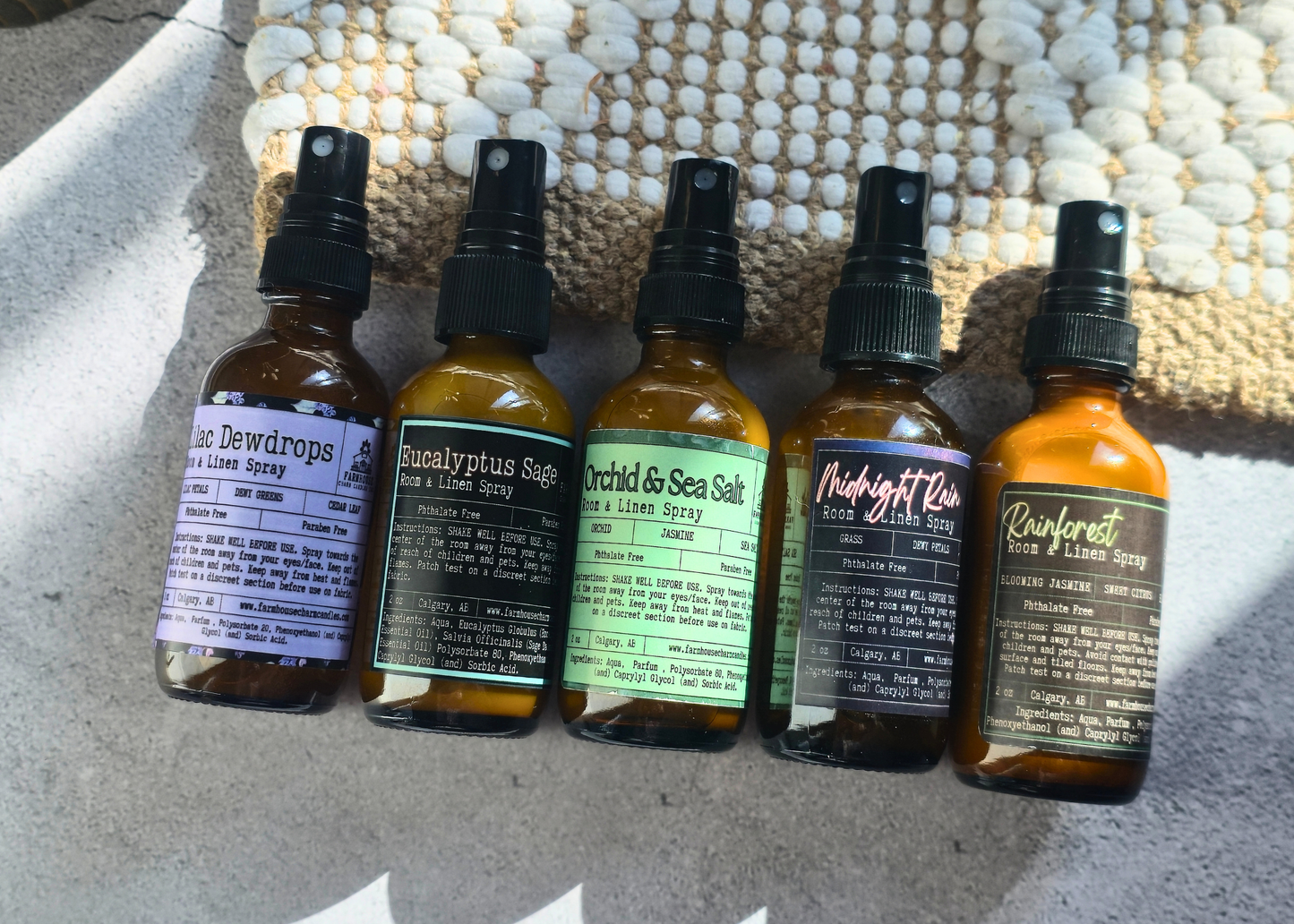 Five amber glass bottles with labels on a textured surface. Farmhouse Charm Candles Room & Linen Spray- Spring collection Bundle