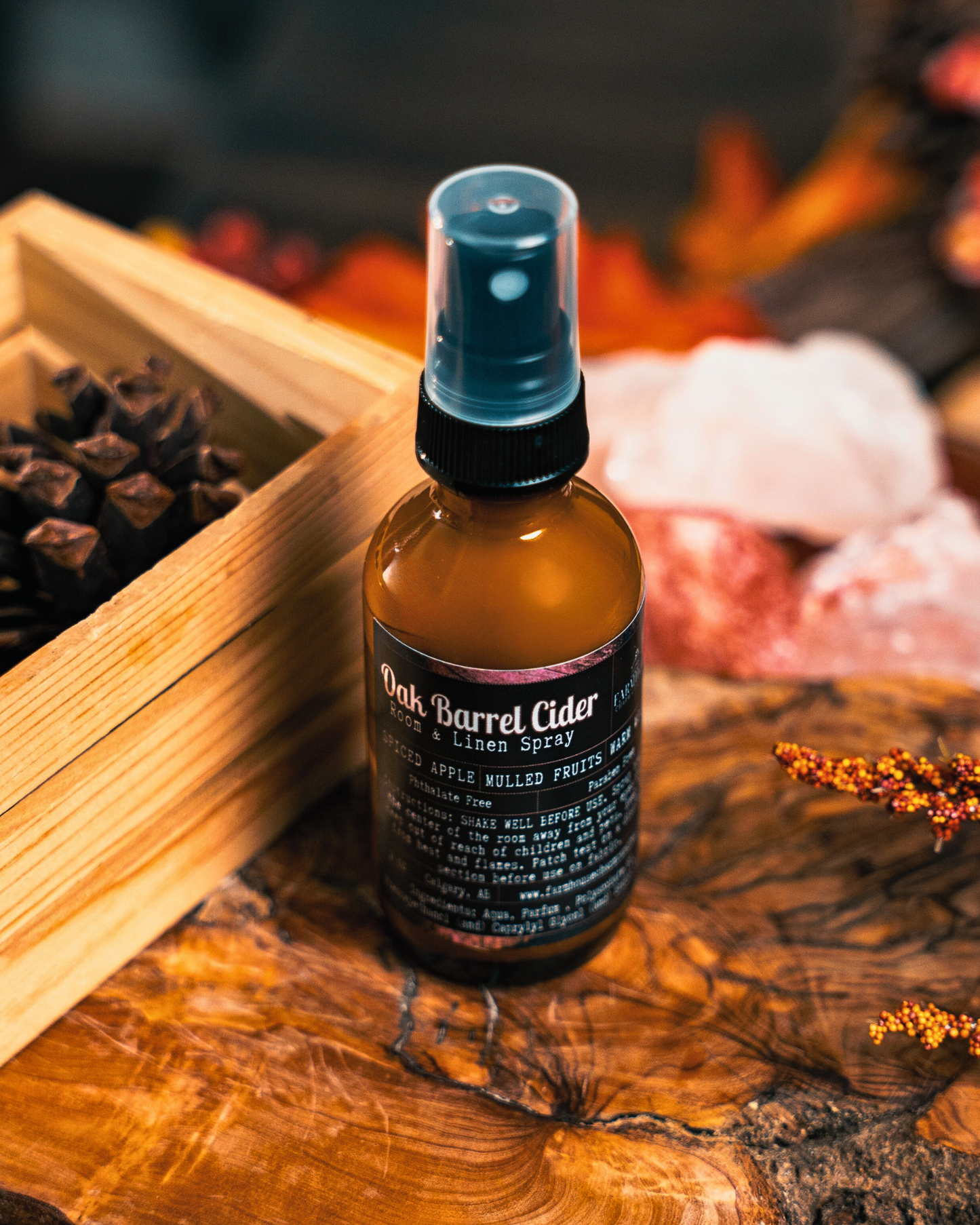 Bottle of Oak Barrel Cider Room & linen spray by Farmhouse Charm Candles on a wooden surface with a fall themed background.