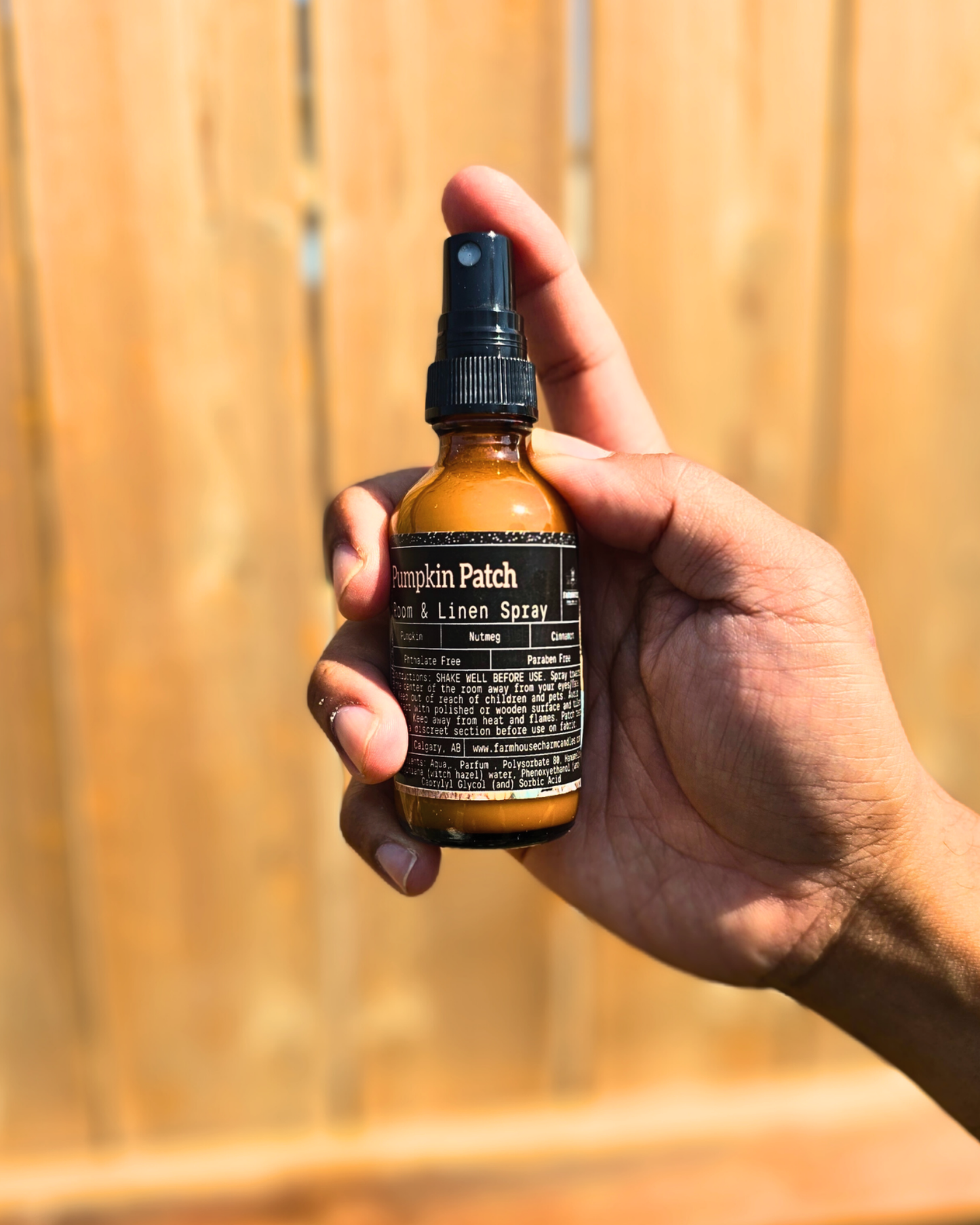 Hand holding a bottle of 'Pumpkin Patch' room & linen spray by Farmhouse Charm Candles against a wooden background