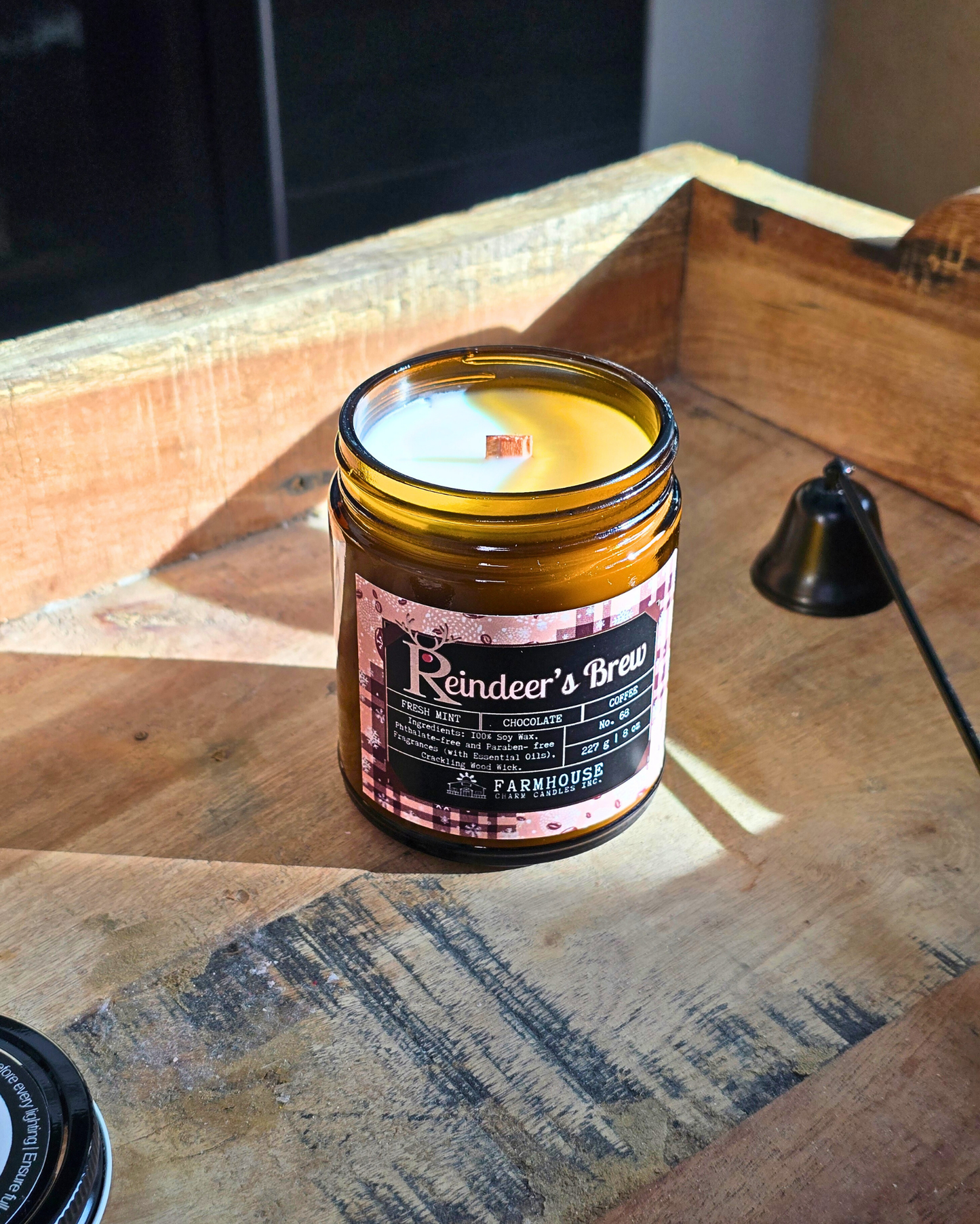 Reindeer’s Brew soy candle in amber jar with warm holiday glow, surrounded by coffee beans, peppermint, and chocolate pieces — cozy Christmas scent from Farmhouse Charm Candles.