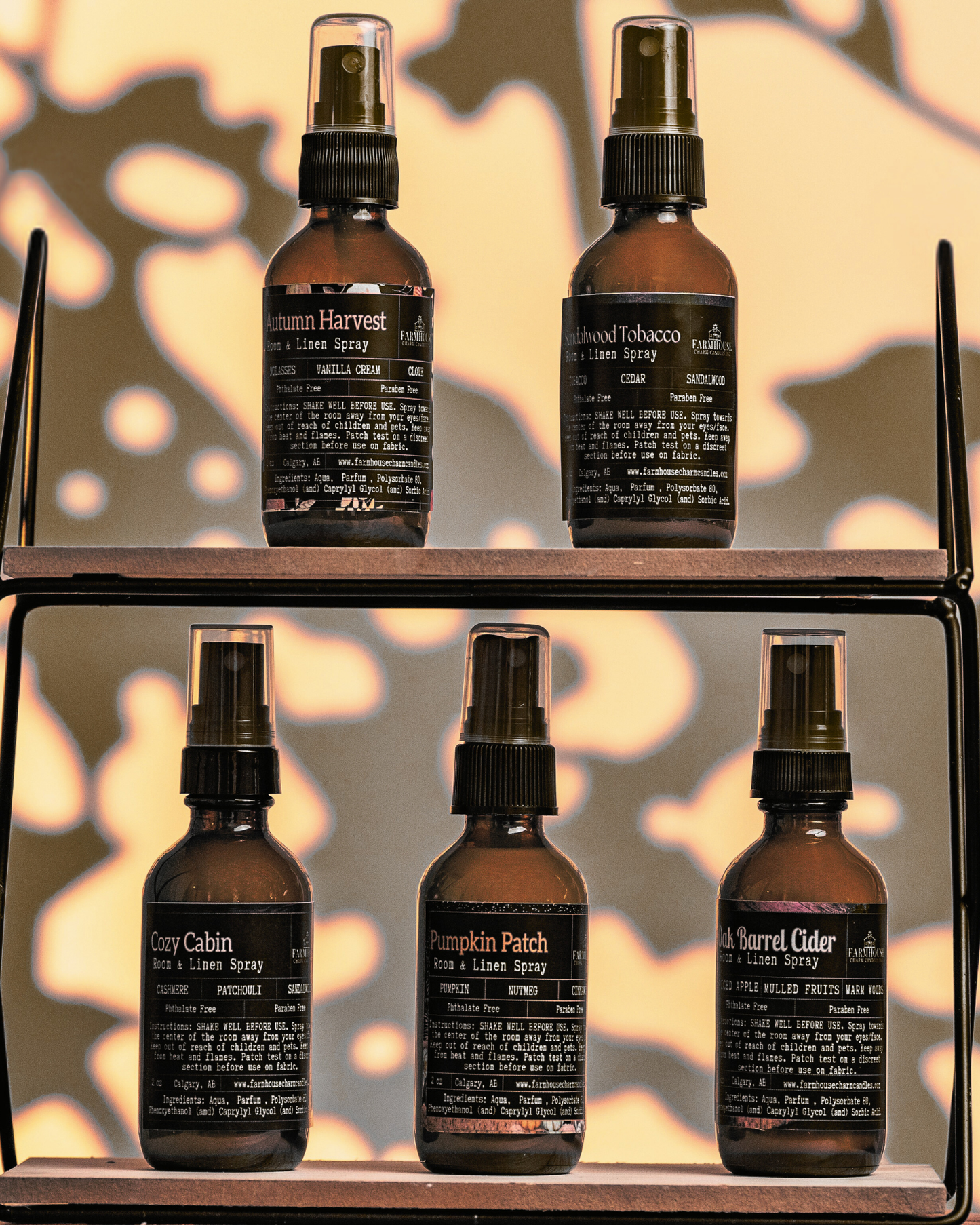 Set of five brown room & linen spray bottles by Farmhouse Charm Candles with labels on a wooden shelf against a leafy background