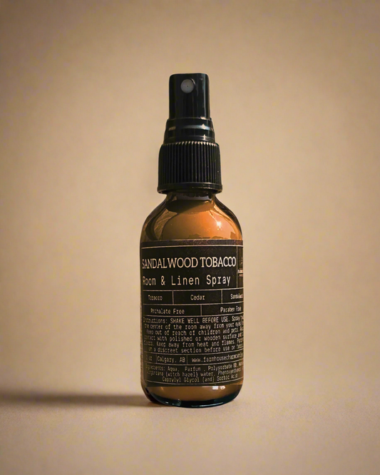 Bottle of Sandalwood Tobacco Room & Linen Spray by Farmhouse Charm Candles on a beige background.