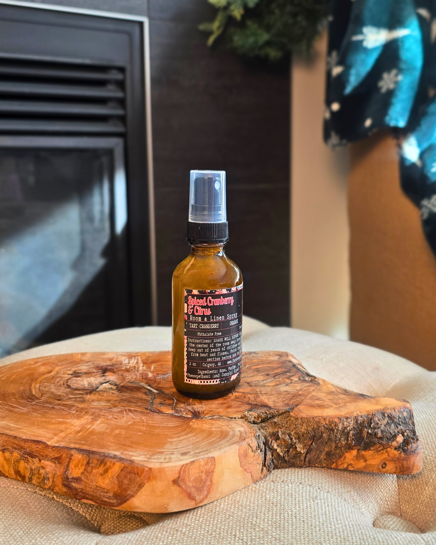 Amber glass bottle of Spiced Cranberry & Citrus Room and Linen Spray placed on a rustic wooden surface with holiday accents — evokes a warm, cozy Christmas scent of cranberry, orange, and cinnamon.
