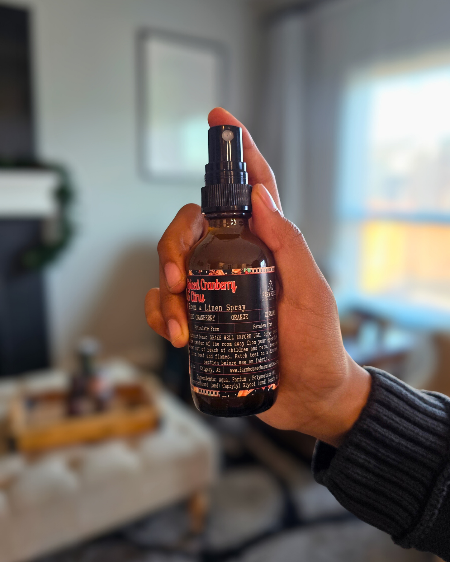 Hand holding an amber glass bottle of Spiced Cranberry & Citrus Room and Linen Spray — evokes a warm, cozy Christmas scent of cranberry, orange, and cinnamon.
