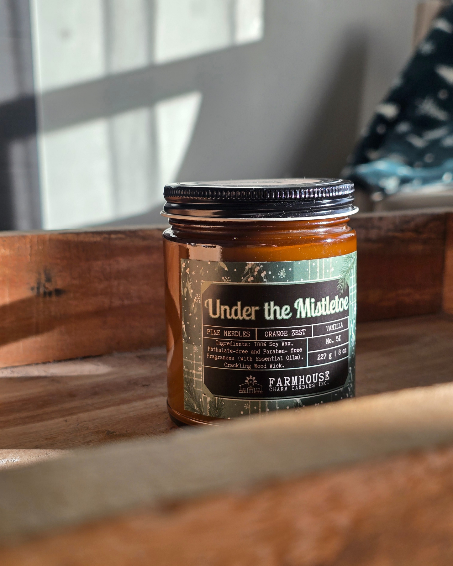 Candle in a glass jar with a label Under the Mistletoe by Farmhouse Charm Candles on a wooden surface