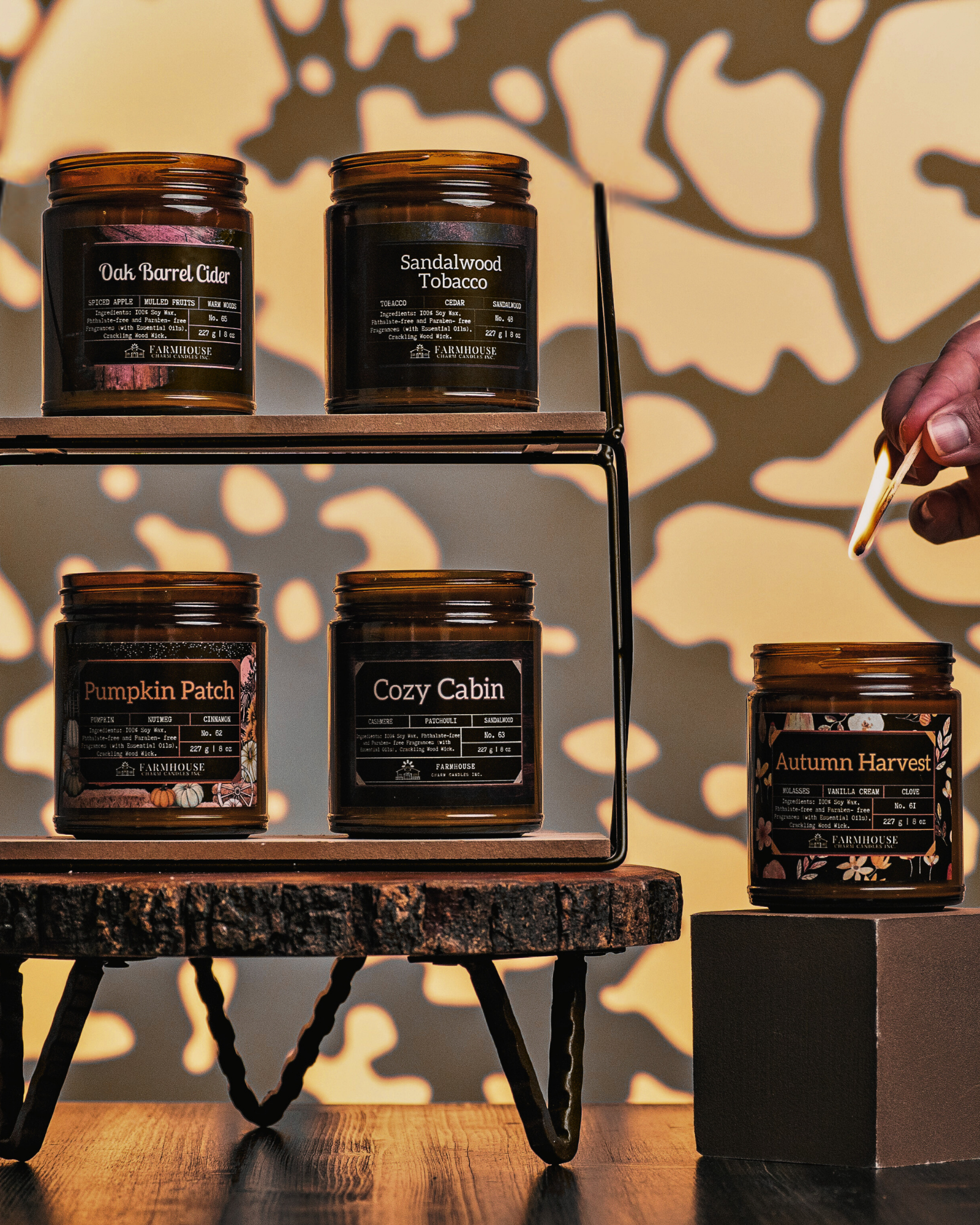 Collection of Autumn Glow Soy candles with labels by Farmhouse Charm Candles on a wooden shelf against a leafy background