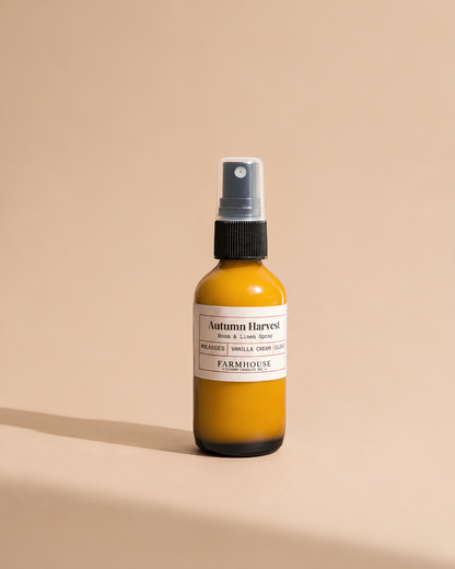 A small amber glass spray bottle with a white label reading 'Autumn Harvest' by Farmhouse Charm Candles on a warm beige background.