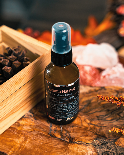 Bottle of 'Autumn Harvest' room &  spray by Farmhouse Charm Candles on a wooden surface with fall decorative elements.