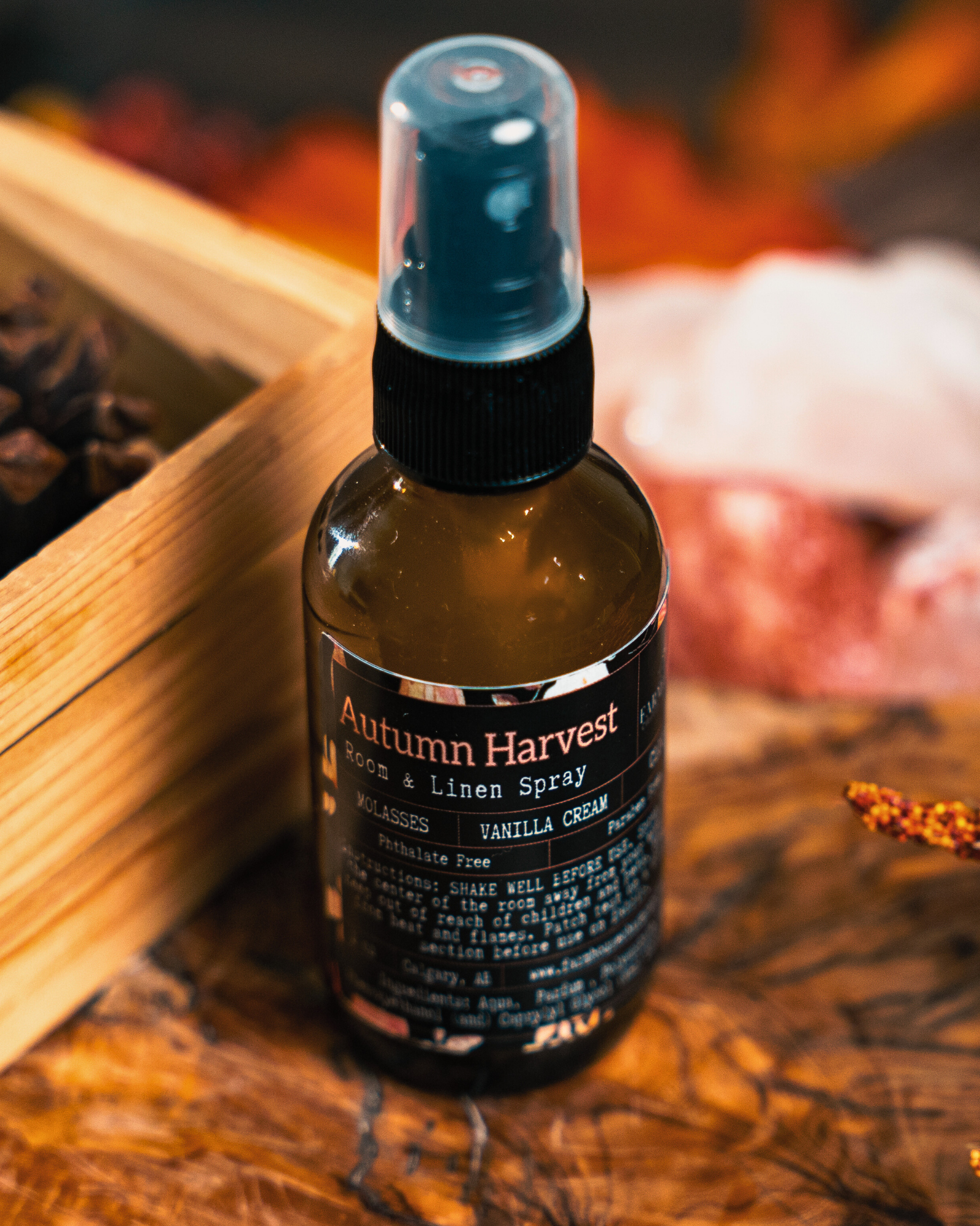 Bottle of 'Autumn Harvest' room  & linen spray by Farmhouse Charm Candles on a wooden surface with blurred background