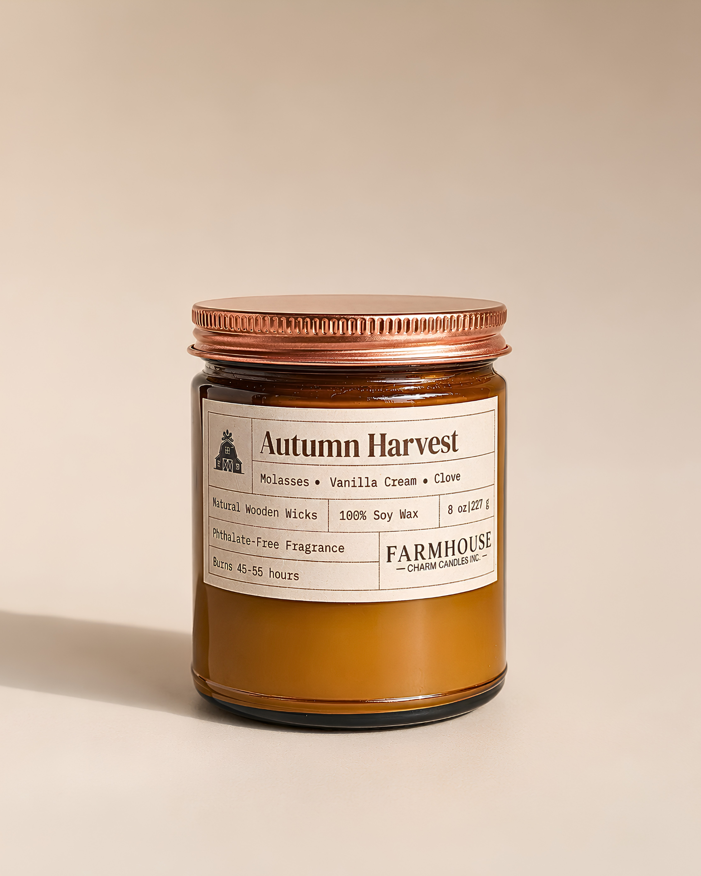 A Farmhouse Candle Company 'Autumn Harvest' scented candle in a amber-colored glass jar and a copper metal lid, set against a solid beige background.