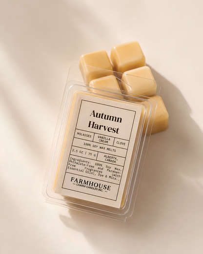A clear plastic clamshell package of  'Autumn Harvest' soy wax melts by Farmhouse Charm Candles , with several pale yellow wax cubes arranged behind it on a warm off-white background.