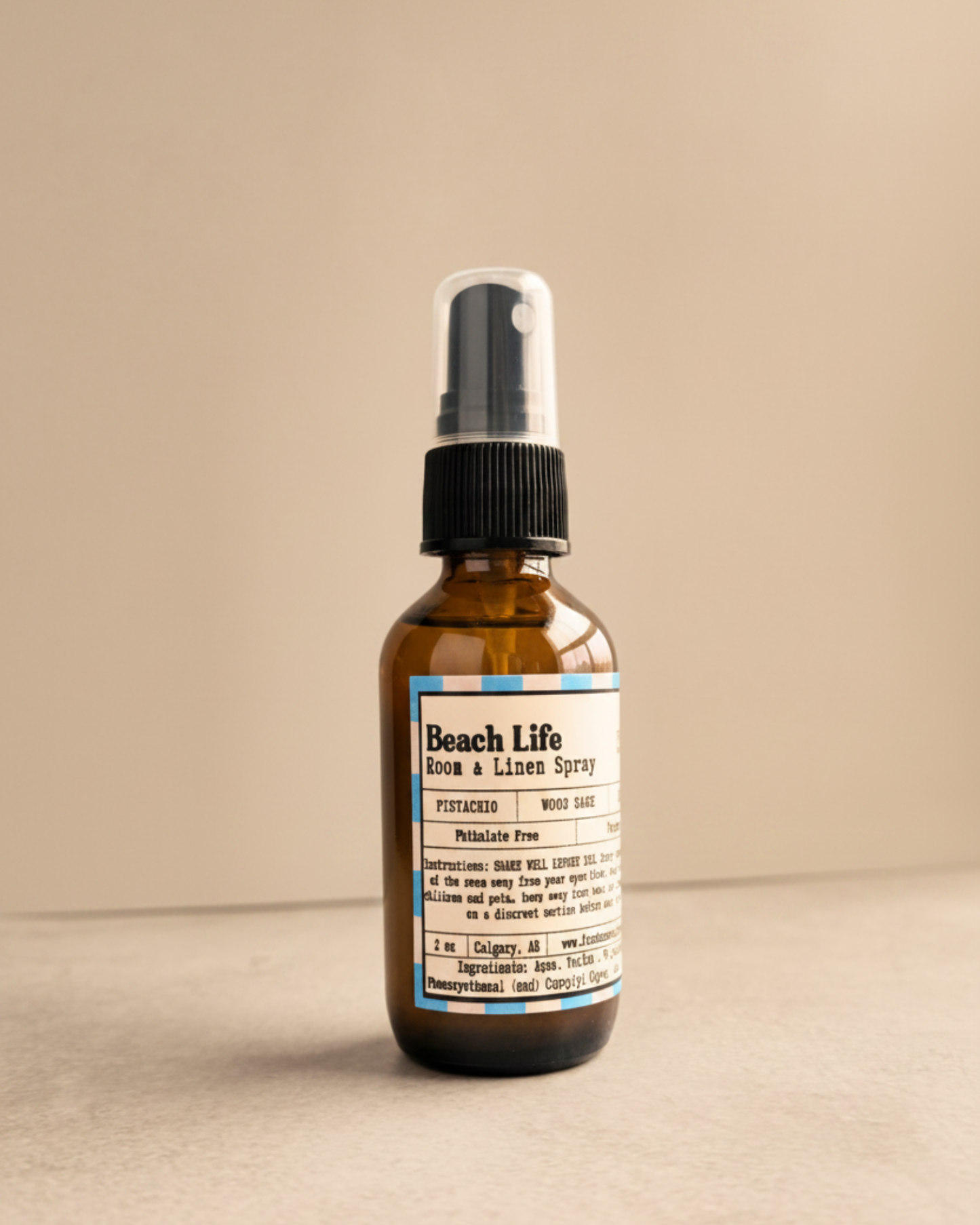 Brown spray bottle labeled 'Beach Life' by Farmhouse Charm Candles on a gray surface with a warm background