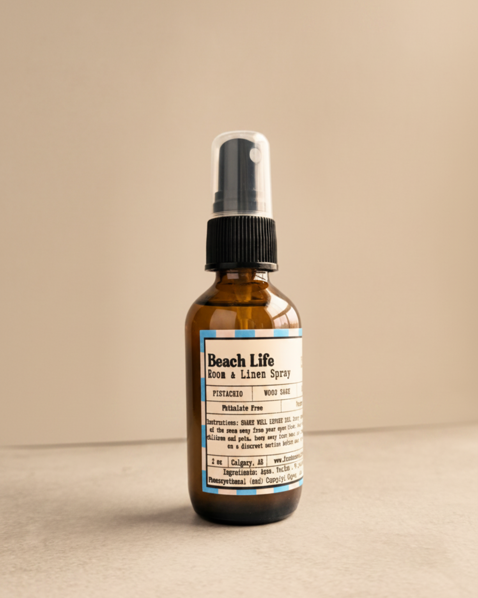 Brown spray bottle labeled 'Beach Life' by Farmhouse Charm Candles on a gray surface with a warm background