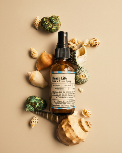 Bottle of 'Beach Life' room and linen spray  by Farmhouse Charm Candles surrounded by seashells on a warm background
