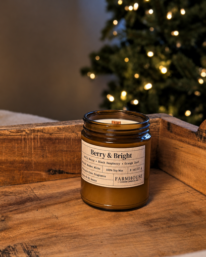 A Farmhouse Charm Candles brand 'Berry & Bright' soy wax candle in a dark amber glass jar, set on a rustic wooden tray with a blurred Christmas tree in the background.