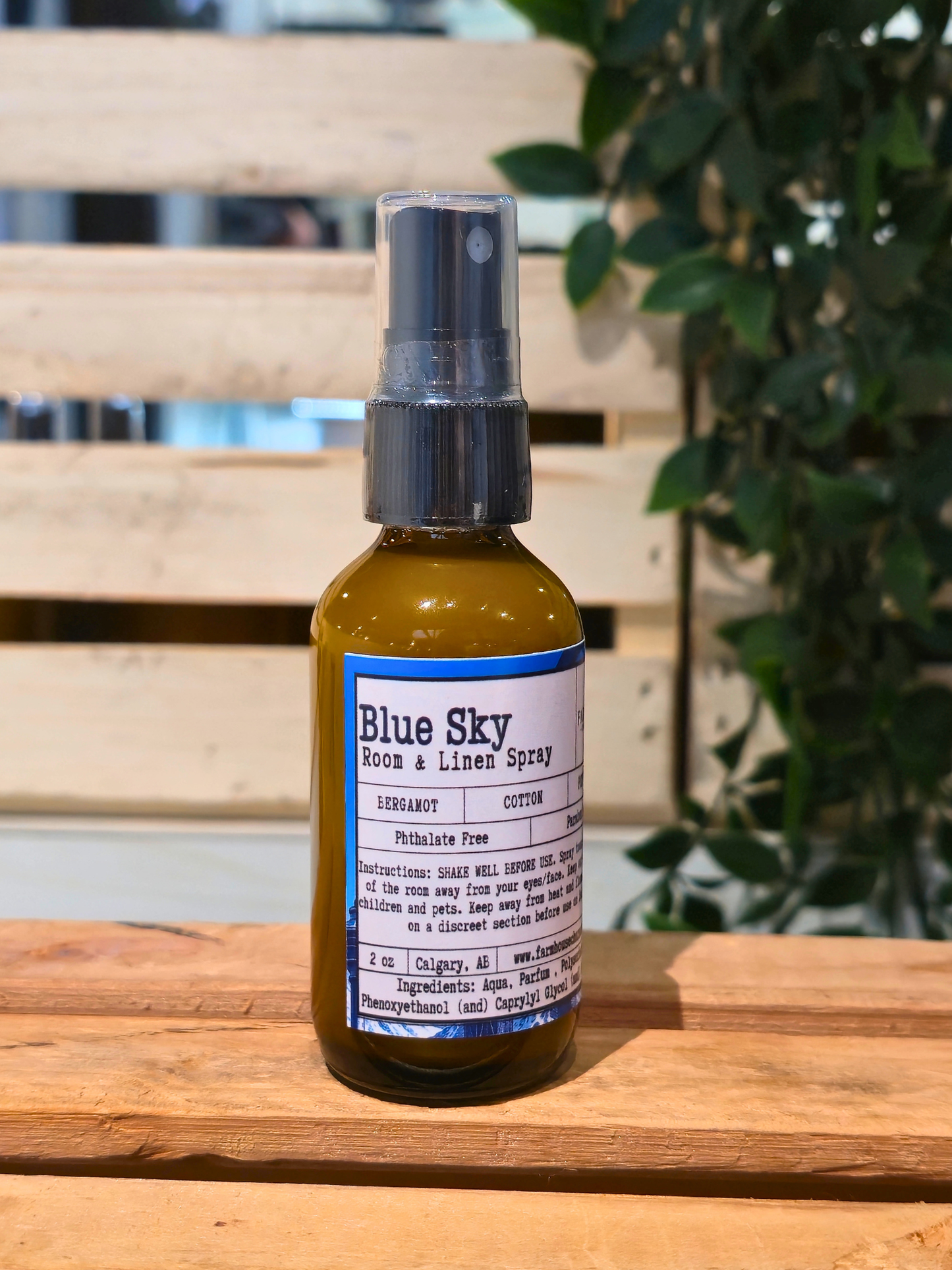 Bottle of Blue Sky Room & Linen Spray by Farmhouse Charm Candles on a wooden surface with a blurred background
