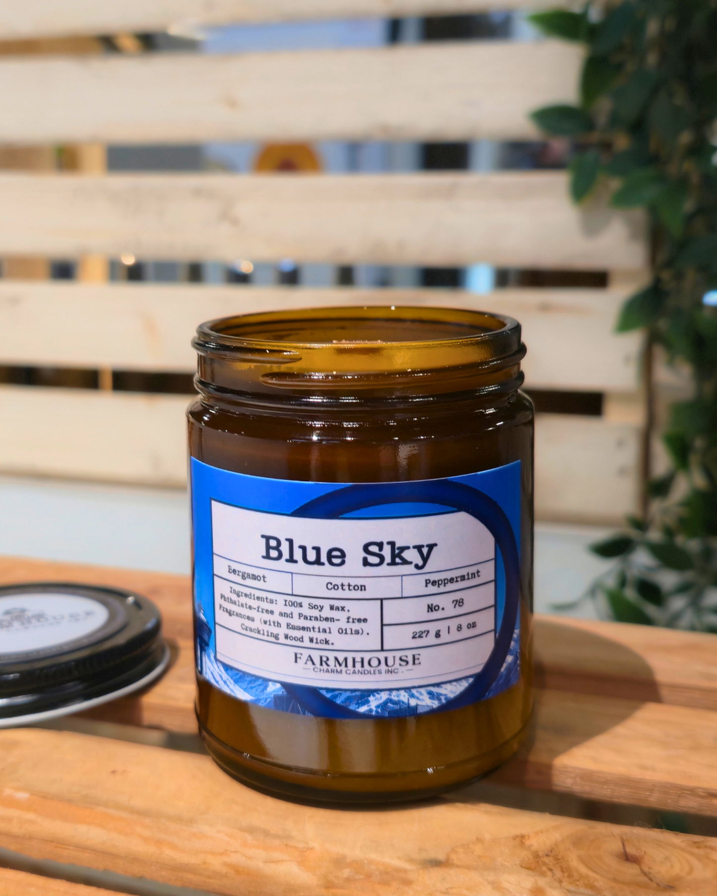 Jar labeled 'Blue Sky' by Farmhouse Charm Candles on a wooden surface with a blurred background