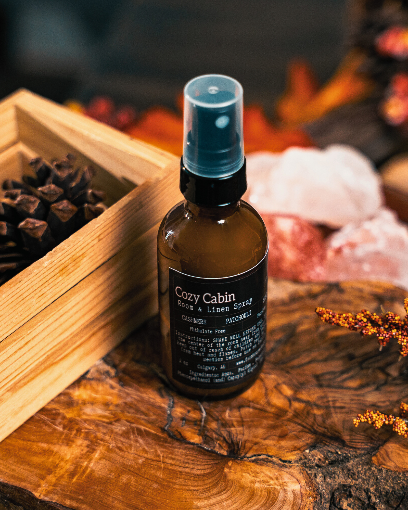 Bottle of Cozy Cabin Room & Linen Spray by Farmhouse Charm Candles on a wooden surface with warm background.