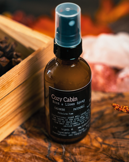Bottle of Cozy Cabin Room & Linen Spray by Farmhouse Charm Candles on a wooden surface