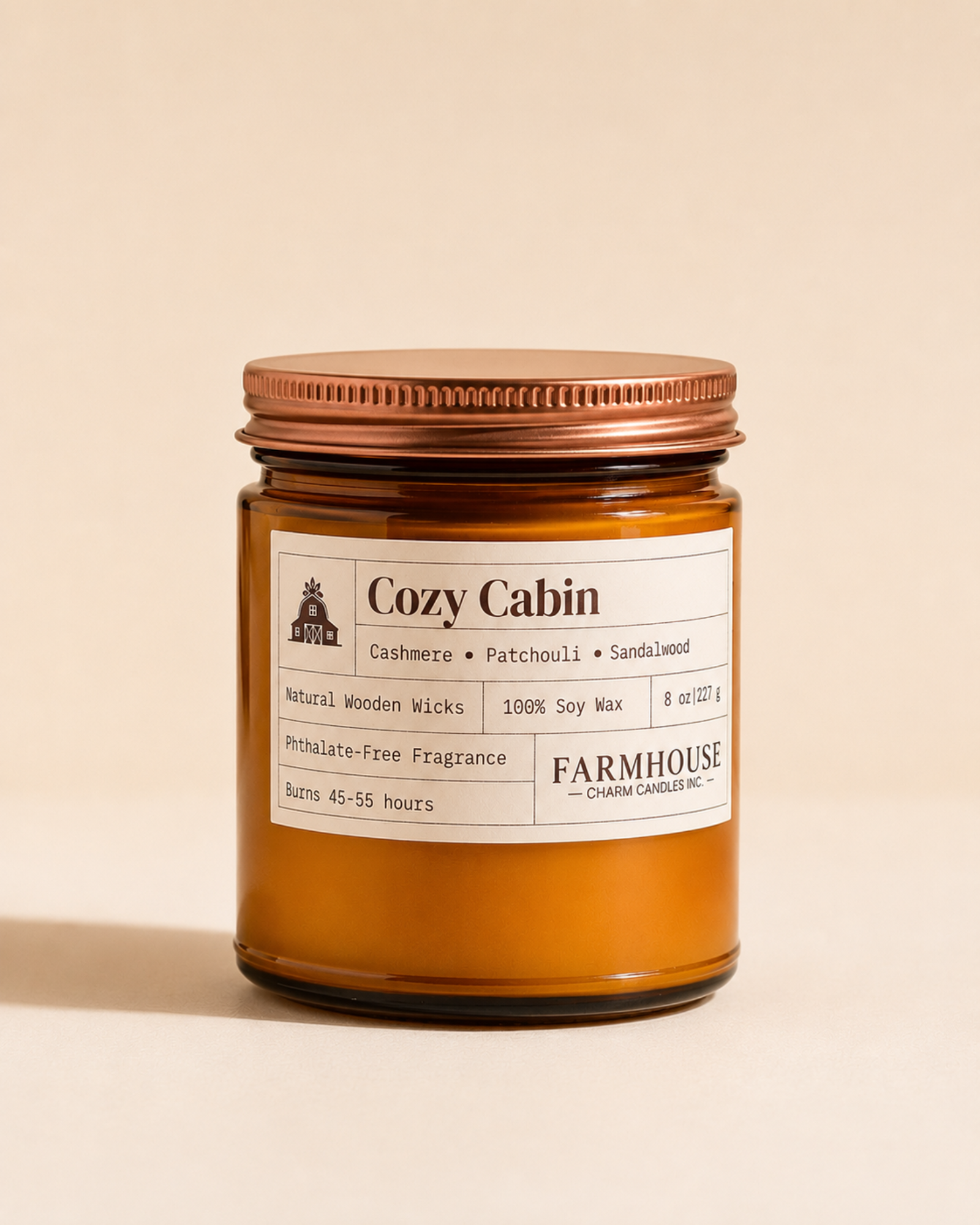 A candle in an amber glass jar with a copper-toned metal lid and a cream-colored label. The label reads 'Cozy Cabin by Farmhouse Charm Candles,  set against a solid beige background.