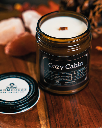 Soy Candle labeled 'Cozy Cabin' by Farmhouse Charm Candles on a wooden surface with decorative elements.