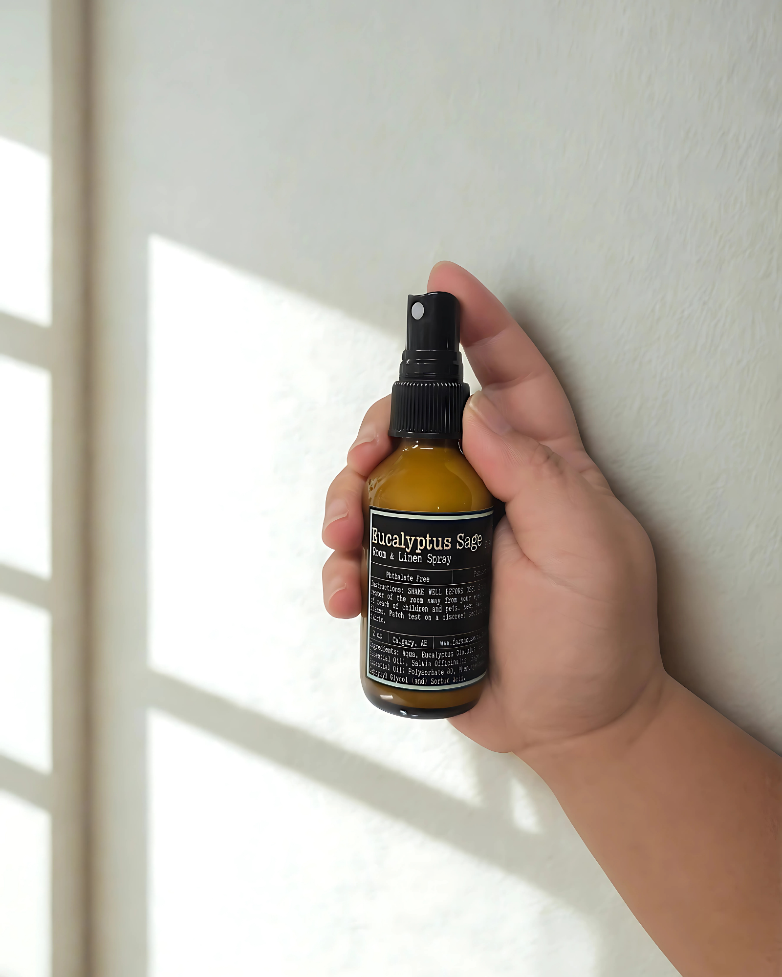Hand holding a bottle of Eucalyptus Sage room & linen spray against a neutral background. Farmhouse Charm Candles