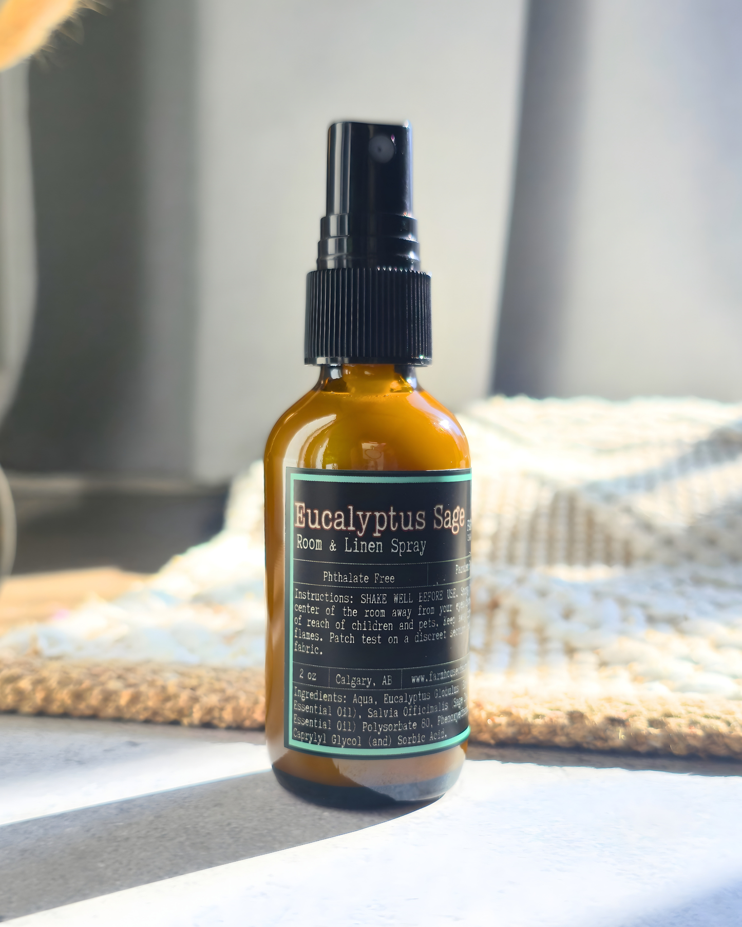 Bottle of Eucalyptus Sage room and linen spray on a wooden surface with a blurred background by Farmhouse Charm Candles