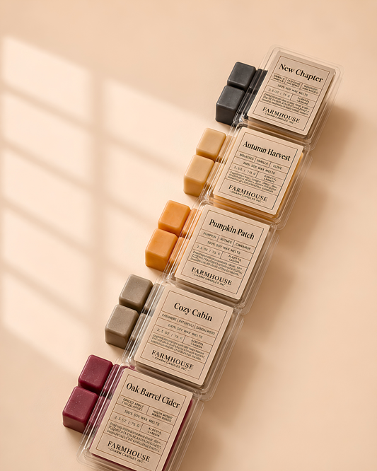 Six small wax melt or scented cube packs arranged diagonally on a warm beige surface. Each clear plastic package contains several wax cubes and a cream label with the brand FARMHOUSE Charm Candles and scent names including New Chapter, Autumn Harvest, Pumpkin Patch, Cozy Cabin, and Oak Barrel Cider.