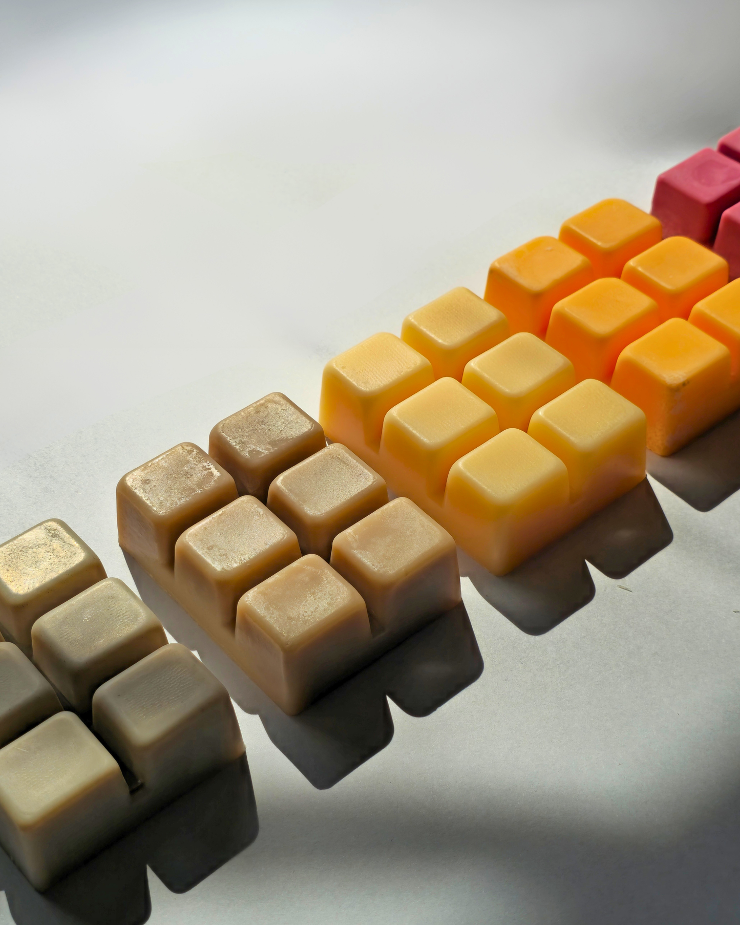 A close-up diagonal arrangement of small square plastic pieces in multiple colors, including cream, beige, yellow, orange, and pink, on a light gray background. Fall Wax Melts Bundle by FARMHOUSE Charm Candles