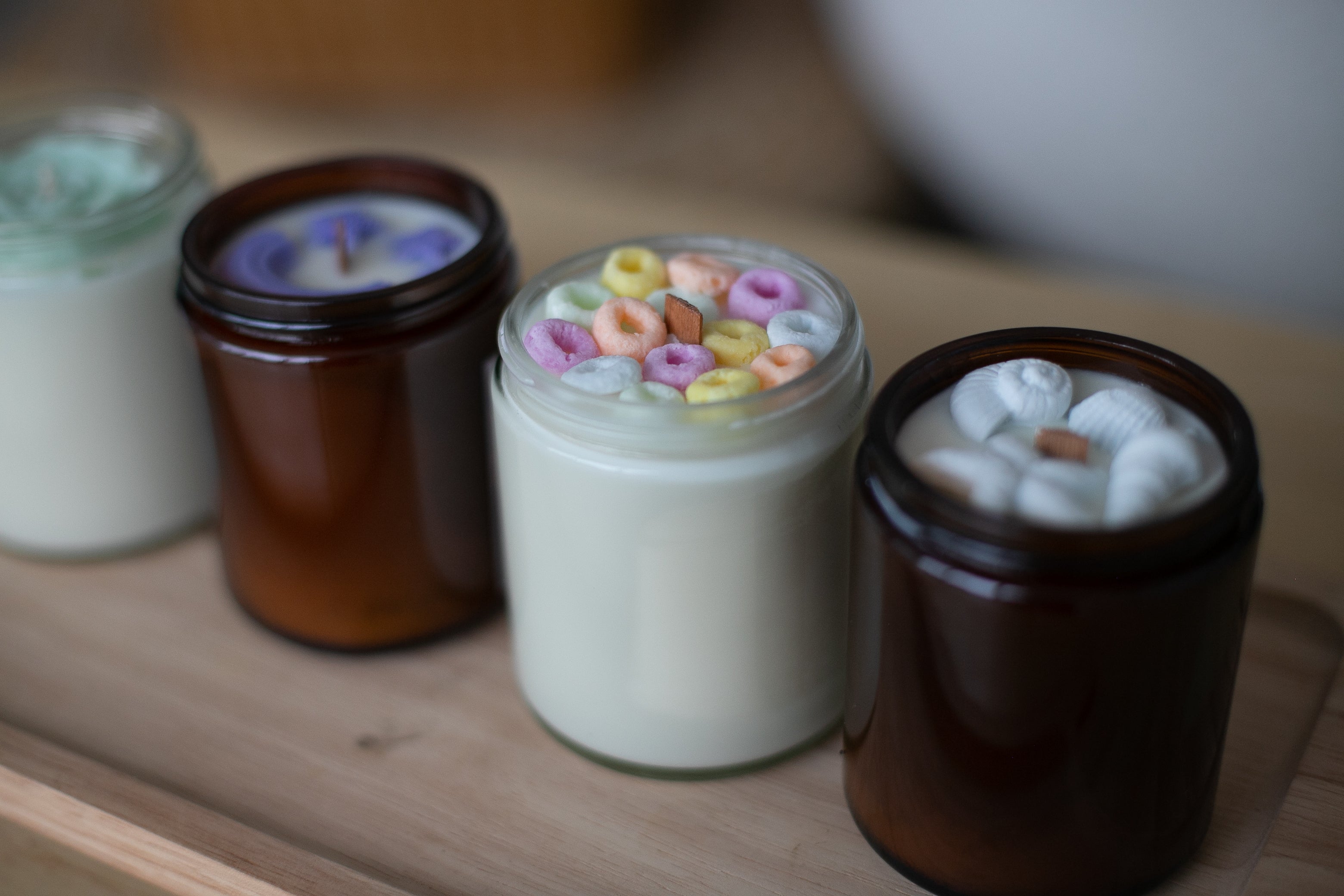 Four small jars with decorative candles on a wooden surface by Farmhouse Charm Candles