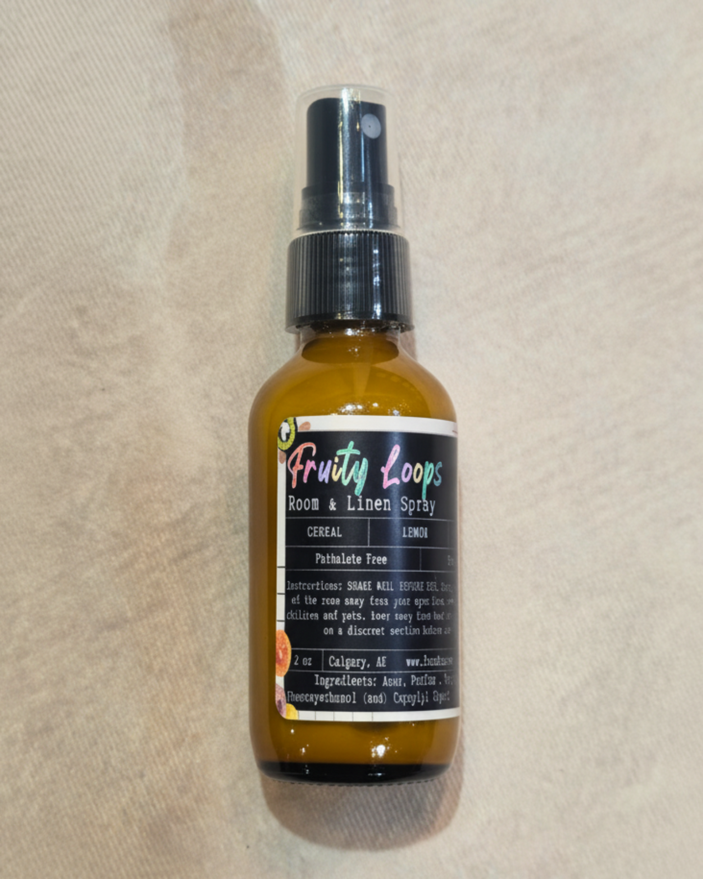 Bottle of 'Fruity Loops' room and linen spray by Farmhouse Charm Candles on a textured beige surface