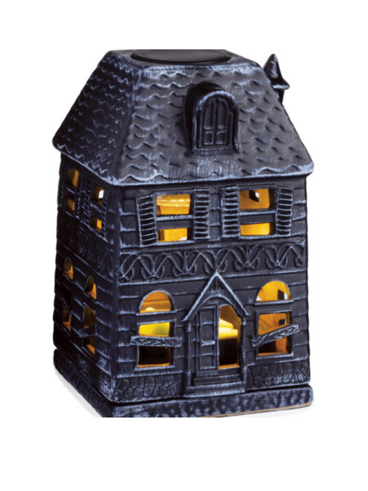 Porcelain Haunted House Illumination Fragrance Warmer with boarded-up windows casting a soft glow. Designed to safely melt wax melts and fill the home with autumn scents. Features a spooky haunted mansion design, includes a warming bulb, and operates with a 3 ft cord and on/off switch. Perfect for Halloween and fall décor. www.farmhousecharmcandles.com