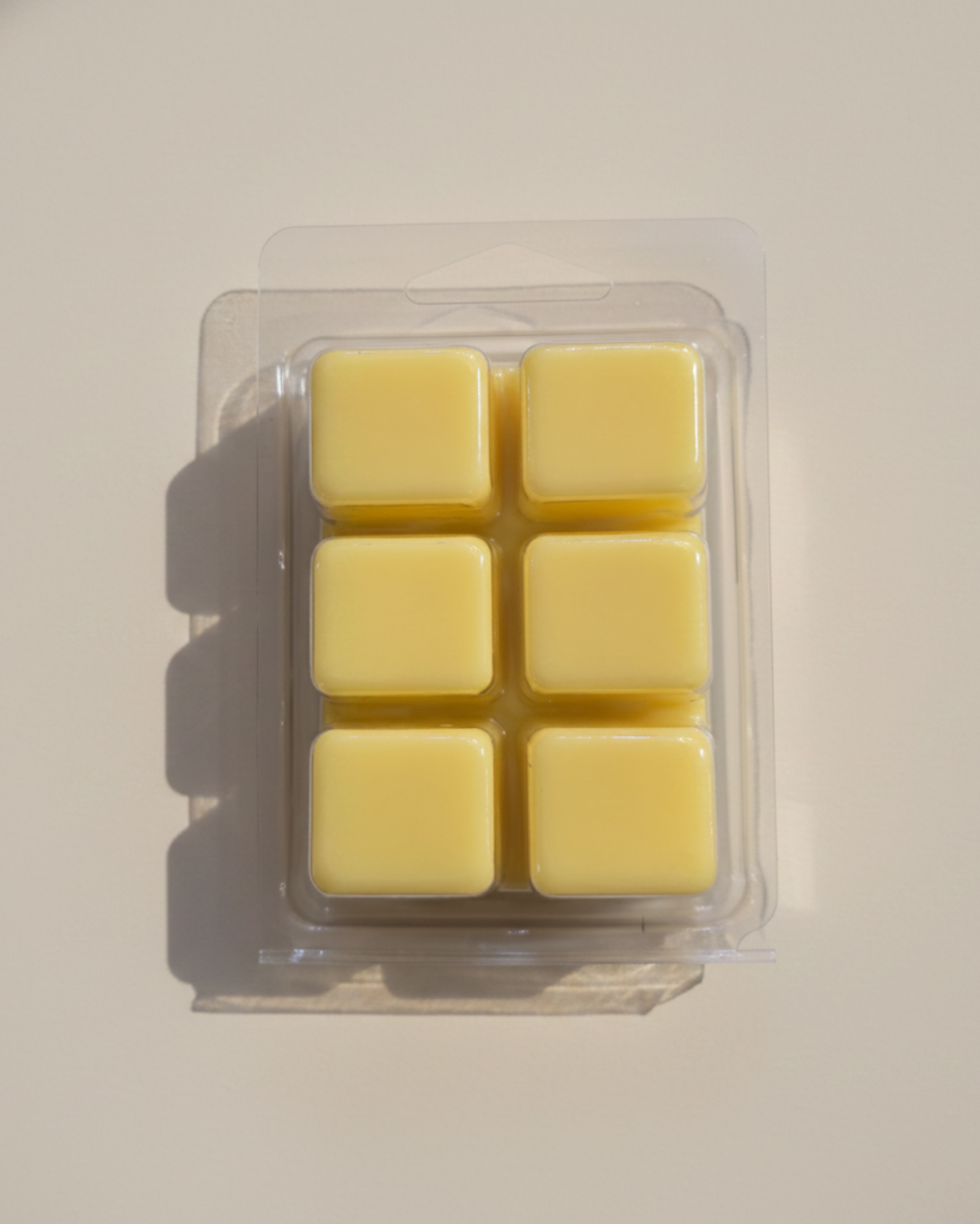 Clear plastic container with six yellow wax cubes on a white background by Farmhouse Charm Candles
