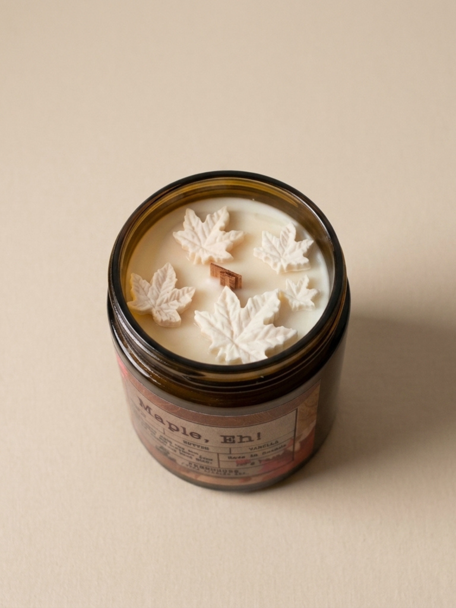 Candle jar with leaf-shaped wax pieces on a beige background. Maple, Eh Soy Candle by Farmhouse Charm Candles