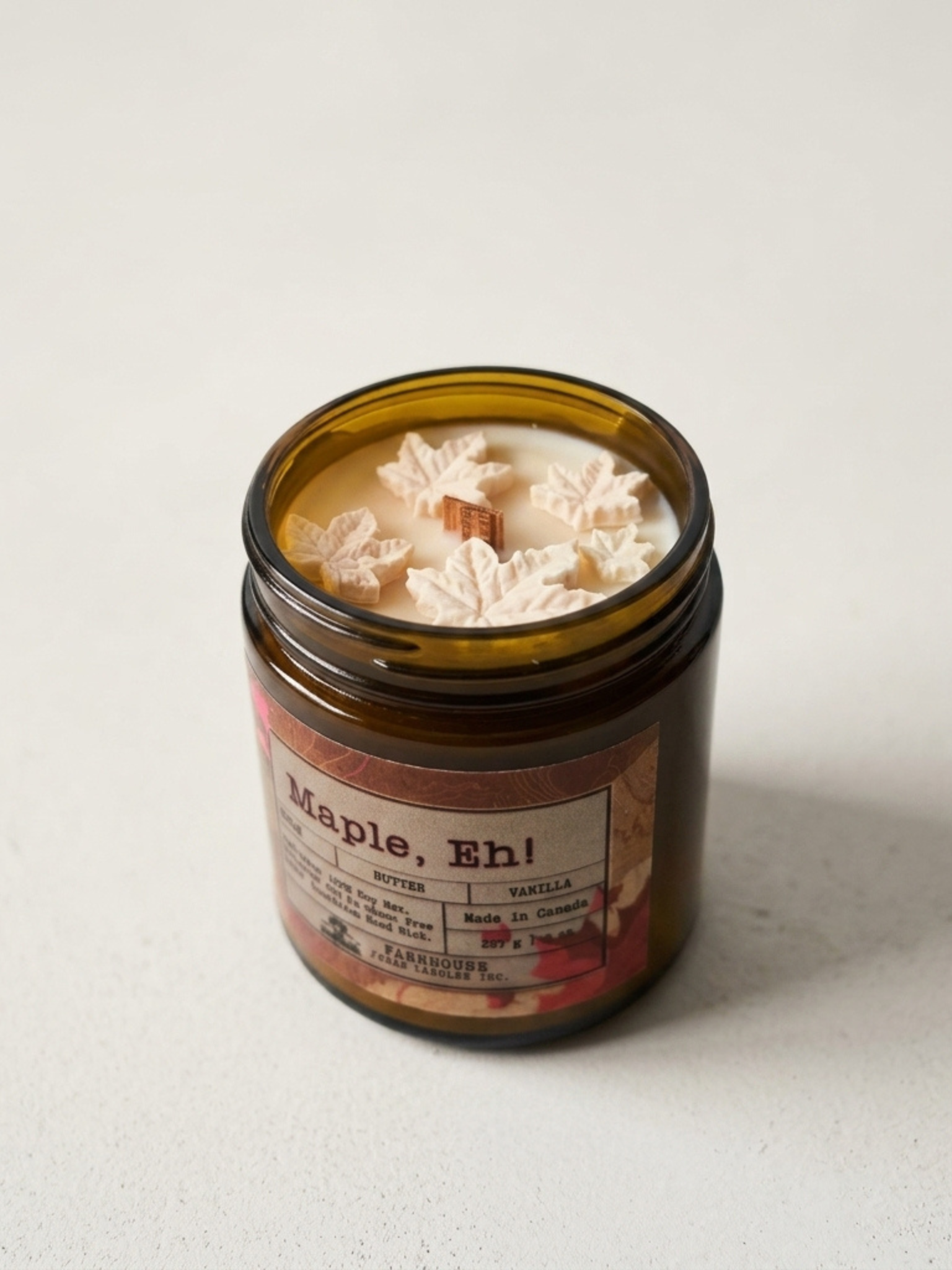 Candle in a glass jar labeled 'Maple, Eh!' by Farmhouse Charm Candles on a light background