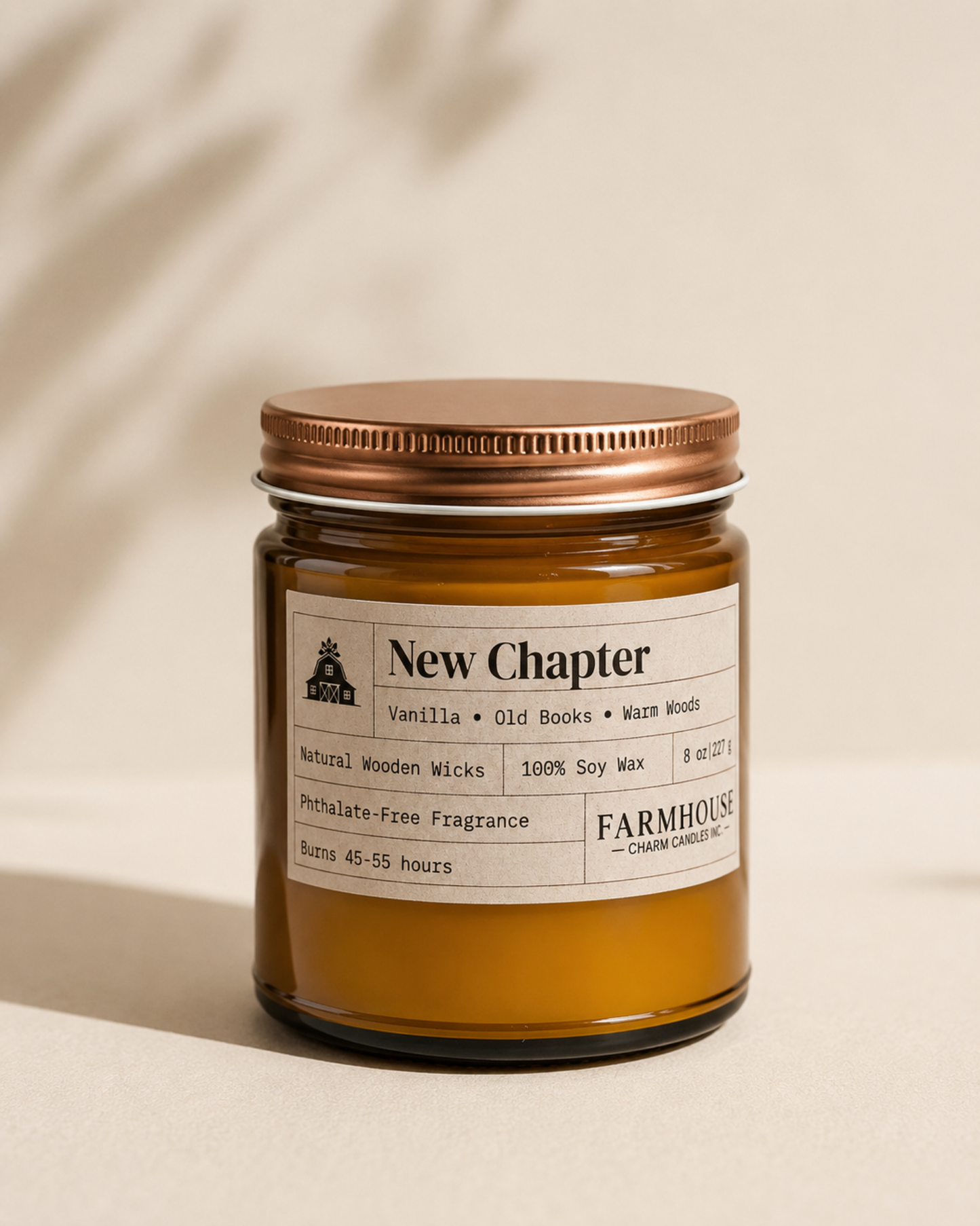 An amber glass jar candle with a metallic copper-toned screw-on lid and a cream paper label reading 'New Chapter' by Farmhouse Charm Candles, set against a warm beige background with soft leaf shadows.