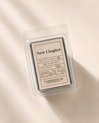 A wax melt package in a clear plastic clamshell container, photographed from above on a warm cream background with soft diagonal shadows. The label reads 'New Chapter' by Farmhouse Charm Candles