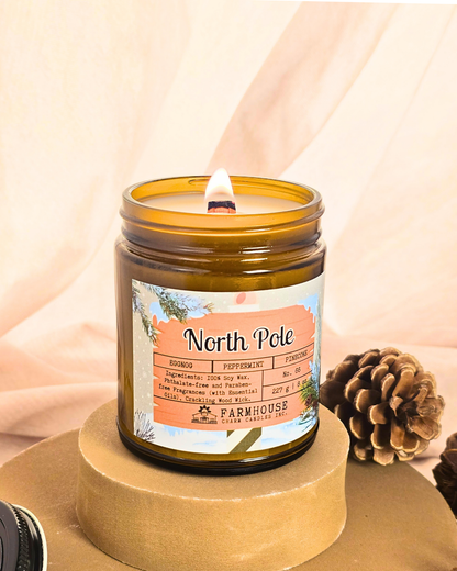 North Pole Soy Candle by Farmhouse Charm Candles — hand-poured soy candle in amber jar with a cozy holiday scent of eggnog, peppermint, and pinecone, styled with festive winter decor.