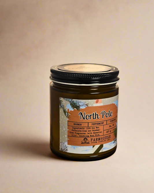 North Pole Soy Candle by Farmhouse Charm Candles — hand-poured soy candle in amber jar with a cozy holiday scent of eggnog, peppermint, and pinecone, styled with festive winter decor.