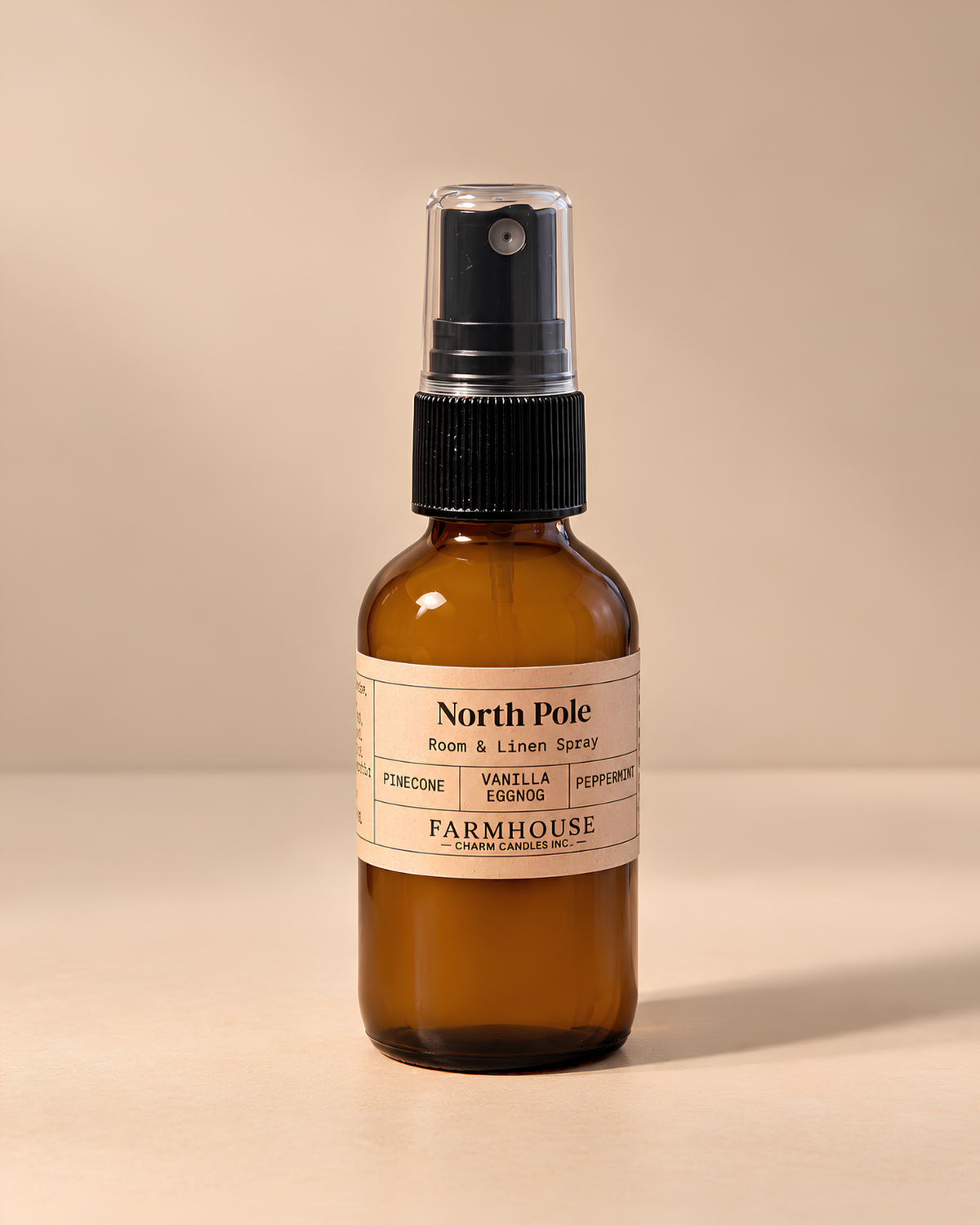 An amber glass spray bottle with a black pump dispenser and a cream-colored label reading 'North Pole' by Farmhouse Charm Candles photographed against a solid beige background.
