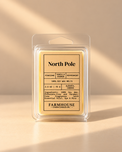 A packaged wax melt product labeled North Pole by Farmhouse Charm Candles in a clear plastic clamshell package with a cream-colored label and pale yellow wax inside, photographed on a warm beige background with soft diagonal shadows.