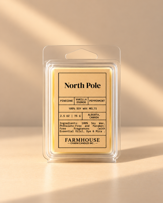 A packaged wax melt product labeled North Pole by Farmhouse Charm Candles in a clear plastic clamshell package with a cream-colored label and pale yellow wax inside, photographed on a warm beige background with soft diagonal shadows.