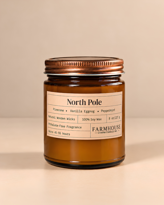 An amber glass jar candle with a copper-toned metal lid and a cream-colored label reading 'North Pole' and 'Farmhouse Charm Candles, photographed against a warm beige background.